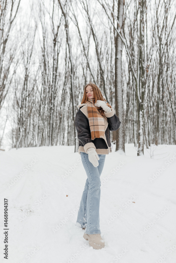 Pretty woman in a fur coat with a big warm scarf around her neck on a winter walk. Woman smiles and rejoices in the snow in winter. Girl walks through a snowy park in winter.