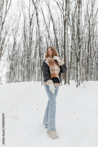 Pretty woman in a fur coat with a big warm scarf around her neck on a winter walk. Woman smiles and rejoices in the snow in winter. Girl walks through a snowy park in winter.