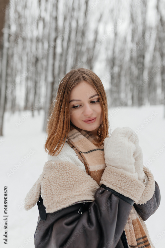 Pretty woman in a fur coat with a big warm scarf around her neck on a winter walk. Woman smiles and rejoices in the snow in winter. Girl walks through a snowy park in winter.