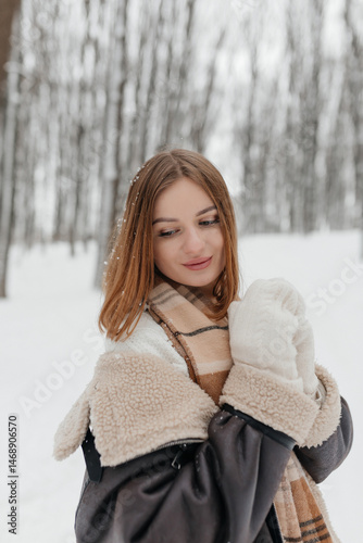 Obraz na płótnie Pretty woman in a fur coat with a big warm scarf around her neck on a winter walk. Woman smiles and rejoices in the snow in winter. Girl walks through a snowy park in winter. w salonie