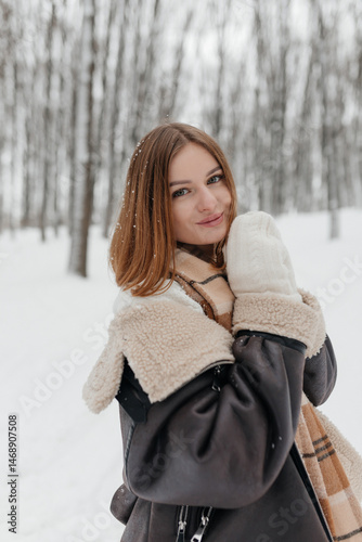 Obraz na płótnie Happy smiling young woman wearing coat, scarf, and mittens enjoying winter weather while walking in snowy winter park. Stylish winter women's clothing. w salonie