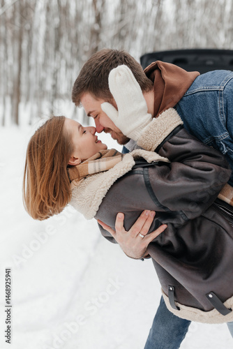Obraz na płótnie A couple in love on a walk in a snowy winter park. A walk in the winter forest of two happy people. A guy and a girl holding hands and hugging. w salonie