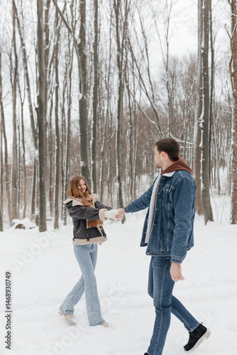 Obraz na płótnie A couple in love on a walk in a snowy winter park. A walk in the winter forest of two happy people. A guy and a girl holding hands and hugging. w salonie