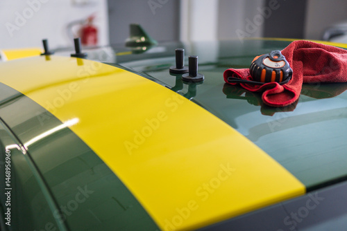 Tools used in the installation of self-adhesive film stickers. Yellow sticker on a green car. Magnets, tape measure and rag used in the installation of decals.