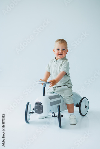 Obraz na płótnie Stylish one-year-old boy in a suit with shorts and a T-shirt rides a car. Toddler boy on a white background with a toy car. w salonie