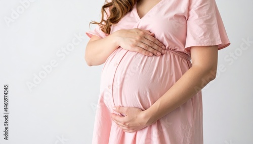 A woman in a pink dress cradles her pregnant belly, symbolizing motherhood and nurturing in a serene setting