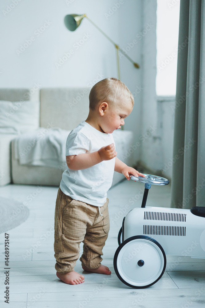 A little one-year-old boy in a t-shirt runs and laughs around the room. A toddler boy is happy and smiling.