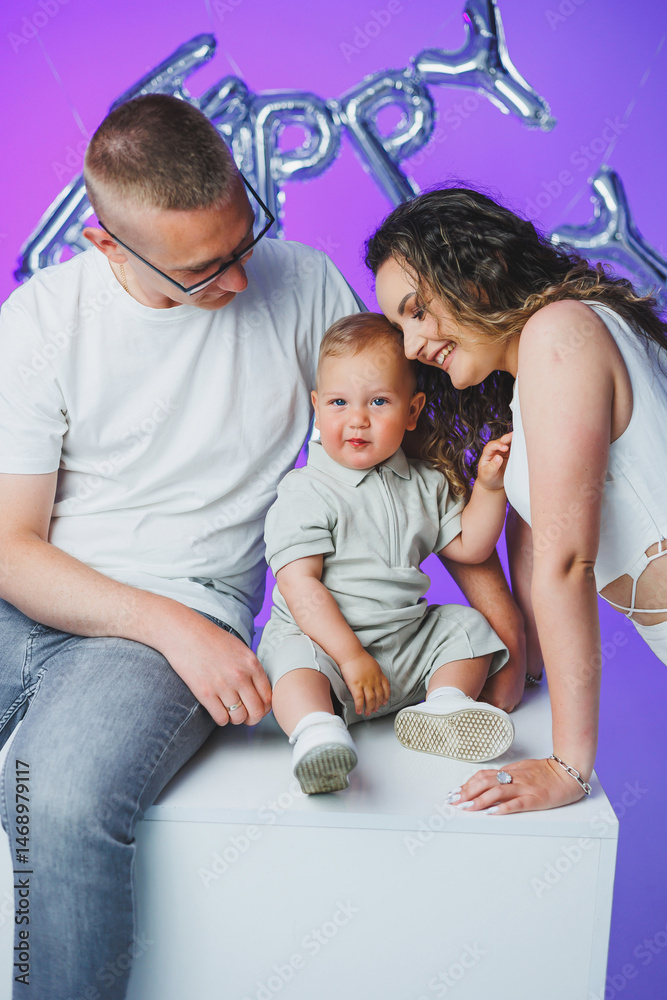 Young mom and dad on a white background playing with their one-year-old son. Toddler boy and mom and dad laughing hugging. Happy mom dad with child.