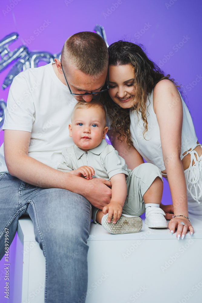 Young mom and dad on a white background playing with their one-year-old son. Toddler boy and mom and dad laughing hugging. Happy mom dad with child.