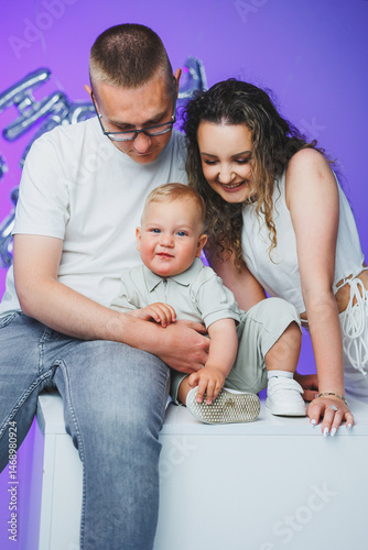 Obraz na płótnie Young mom and dad on a white background playing with their one-year-old son. Toddler boy and mom and dad laughing hugging. Happy mom dad with child. w salonie