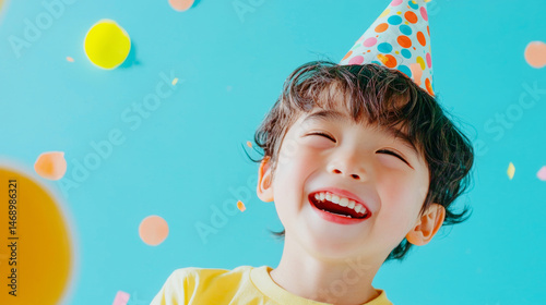 Smiling young asian boy kid wearing party hat happy festive advertising commercial fashion bright celebration blue background