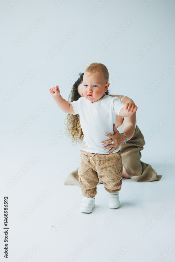 Young mother on a white background playing with her one-year-old son. Toddler boy and mother laughing hugging. Happy mother with child.