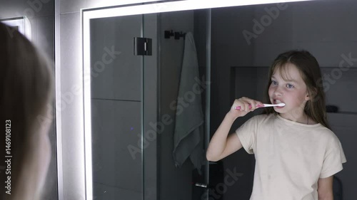 A little girl brushes her teeth before going to bed in front of the bathroom mirror