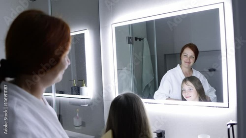 Mom combs her daughter's hair in front of the mirror before going to bed