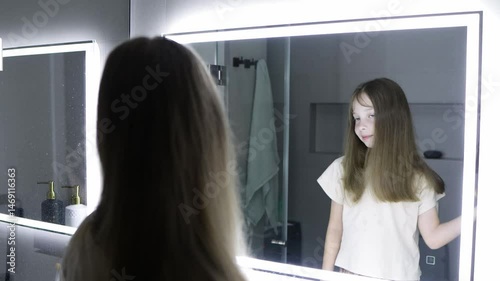 A ten-year-old girl combs her hair before going to bed in front of a mirror