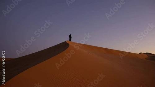Lone explorer walking on sand dune crest at twilight