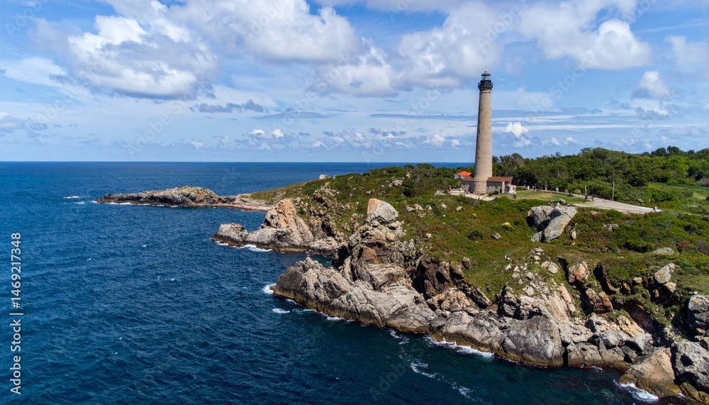 Fototapeta premium Scenic Coastal Lighthouse with Rocky Shoreline and Blue Sky
