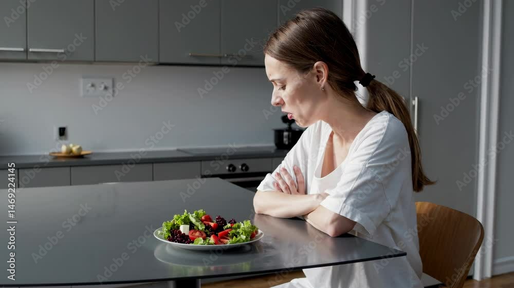 Pensive woman contemplating healthy salad seated in modern kitchen setting Pensive woman contemplating healthy salad seated in modern kitchen setting