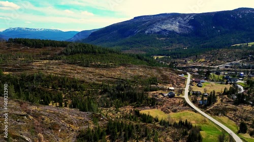 A mountainous landscape with a valley covered with coniferous forests. In the foreground, a rocky slope can be seen under a blue sky.