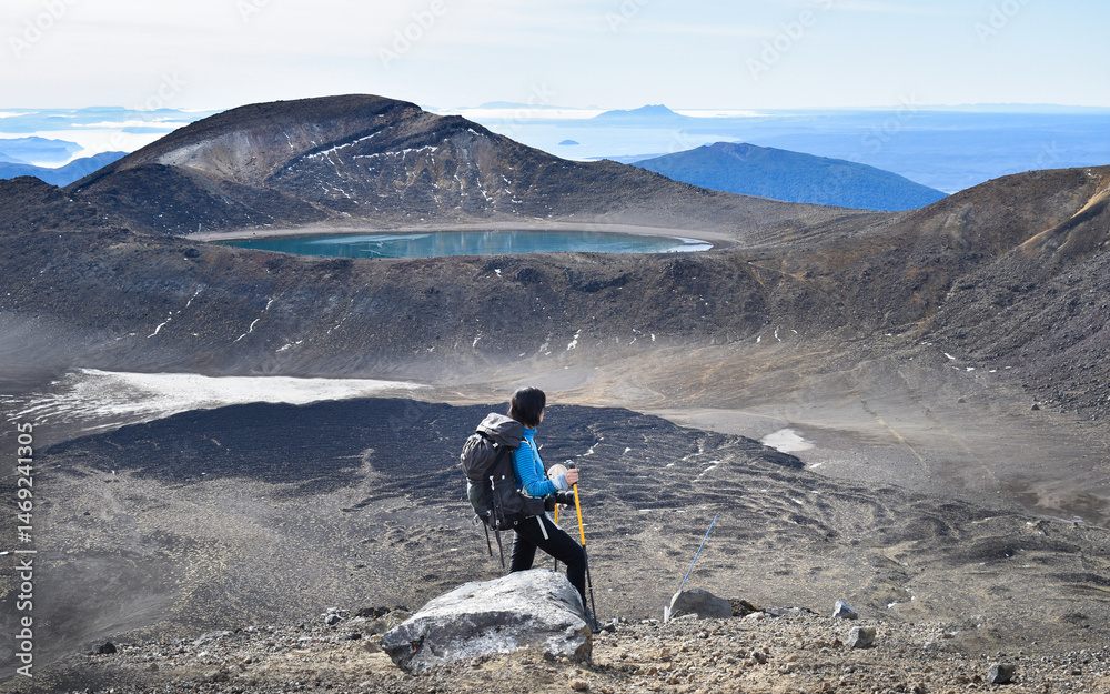 Female backpacker looking at the views of Blue Lake and Mt Taranaki in the far distance. Tongariro Alpine Crossing, Tongariro National Park. New Zealand.