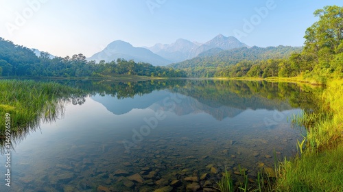 A wide-angle shot of a serene mountain range reflecting in a calm alpine lake, surrounded by lush green forests under a clear sky.