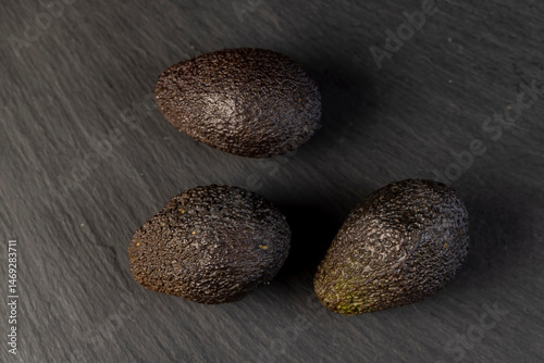 several black avocado fruits of small size on a slate, ripe avocado fruit for cooking, closeup