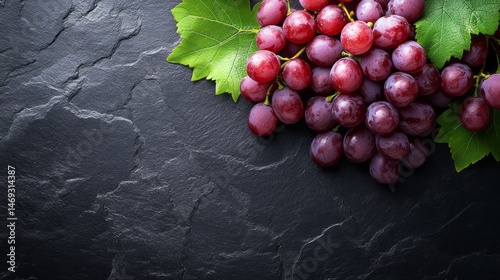 Fresh red grapes on dark slate surface with leaves.