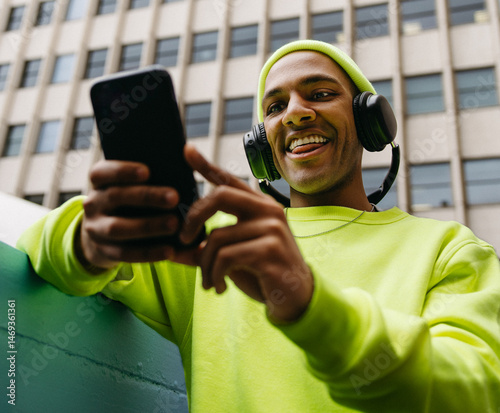 Low angle portrait of young multiracial man using smartphone with headphones in city