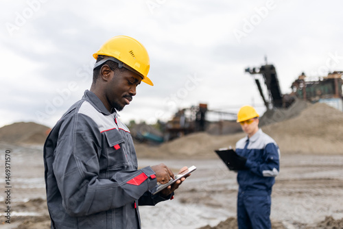 Portrait African man adult surveying engineer use tablet computer for control in sand quarry ore mining with caucasian male adult