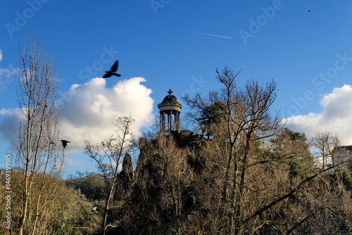 Le temple de la Sybille du parc des Buttes Chaumont avec oiseau  volant dans le ciel bleu. Paris. France.