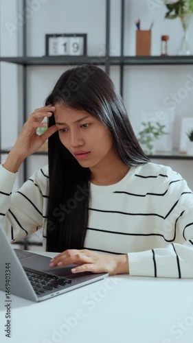 Young asian woman looking tired and stressed while working on laptop at home, showing signs of fatigue, burnout, or mental exhaustion in a home office environment.