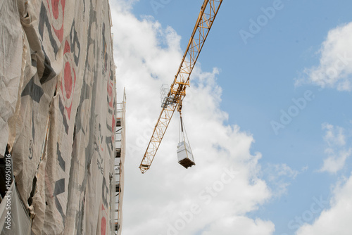 A tall crane on a construction site, blue sky. Construction crane in the sky. Yellow crane tower lifting up