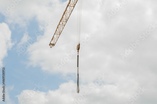 A tall crane on a construction site, blue sky. Construction crane in the sky. Yellow crane tower lifting up