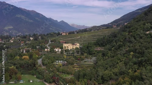 Fernblick auf ein Schloss inmitten einer grünen Hügellandschaft, umgeben von Bergen und Natur, Video, Drohne, Drohnenaufnahme, Gärten von Schloss Trauttmansdorff, Meran, Trentino, Südtirol, Italien