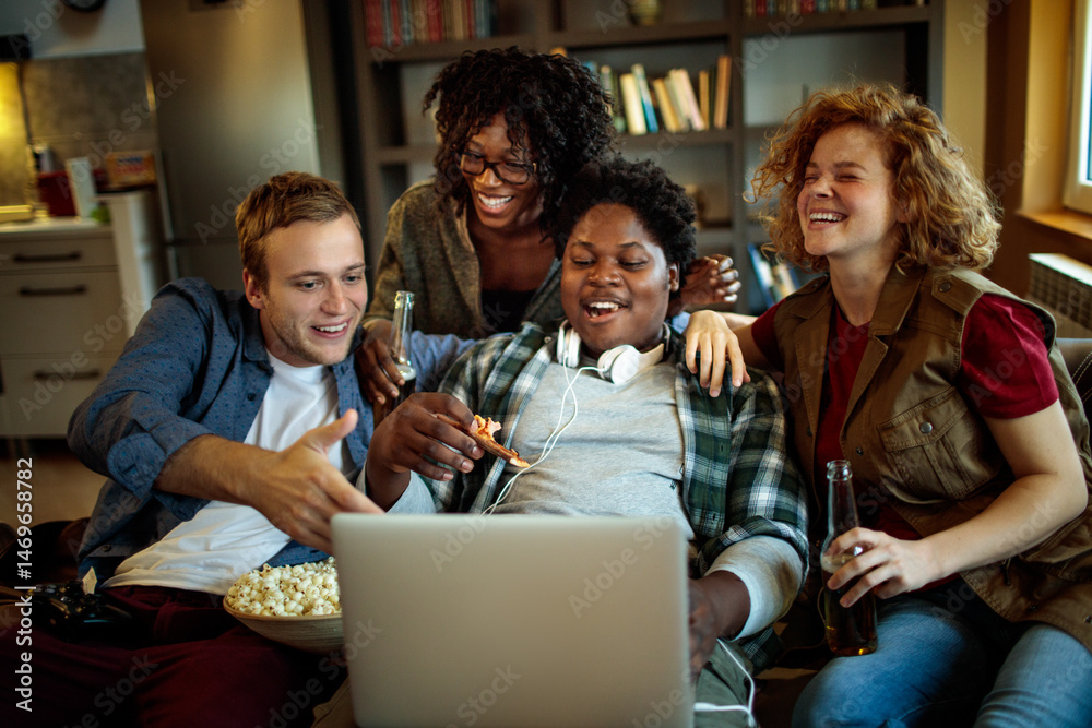Fototapeta premium Young and diverse group of friends watching a movie on laptop in the living room on the couch
