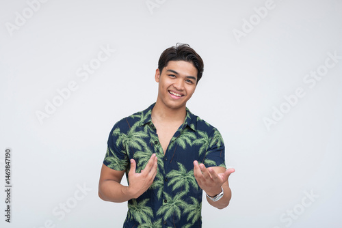 A confident Southeast Asian man in a tropical shirt, smiling and gesturing as if bragging or showing off accomplishments. Isolated on a light background.