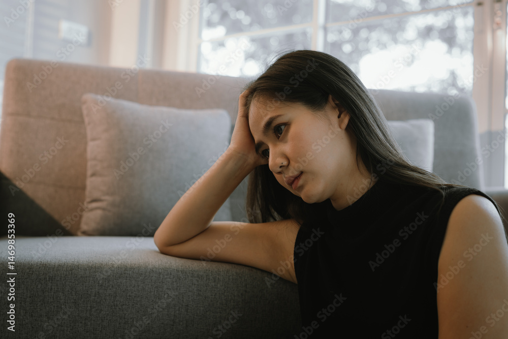 A distressed young adult woman sits alone indoors, experiencing sadness, anxiety, and emotional pain, overwhelmed by grief and stress. A distressed young adult woman sits alone indoors, experiencing sadness, anxiety, and emotional pain, overwhelmed by grief and stress.