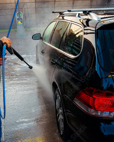 A sleek black car getting a thorough wash with pressurized water and cleaning agents.