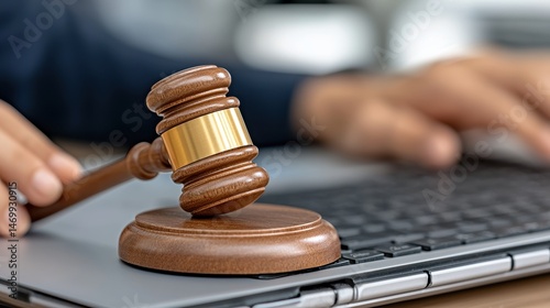 Close up of a wooden gavel resting on a laptop keyboard, with a person's hands typing in the background. The image suggests legal proceedings or