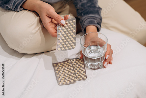 a woman sits on the bed and holds pill packs in her hands and shows the pills to the doctor during an online consultation