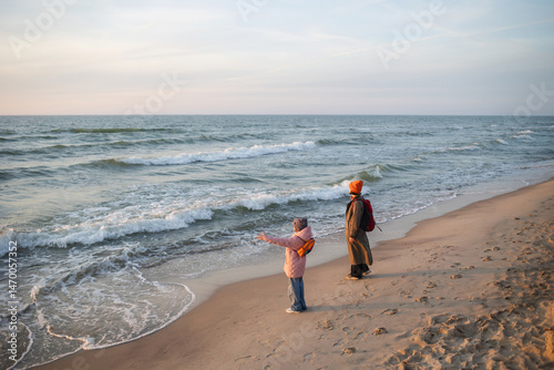 family mother and child walk seashore in spring or autumn in cool weather at sunset. recreation and travel with backpack at sea