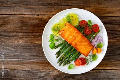 Fried salmon steak with green asparagus, cherry tomatoes and lime on wooden table