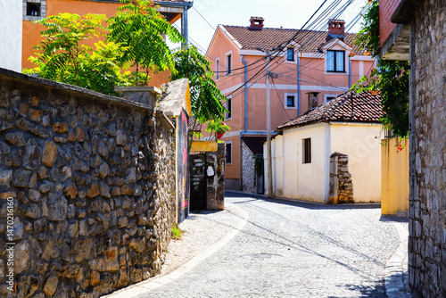 Fototapeta Naklejka Na Ścianę i Meble -  Quiet cobblestone street with private houses and stone walls in Podgorica, sunny day with traditional architecture. Montenegro
