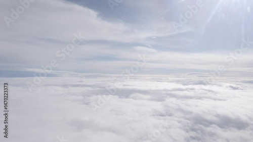 Airplane flight over white cloud and sun beams at sky. Fly in clear soft clouds at sunny light day, looking from plane window