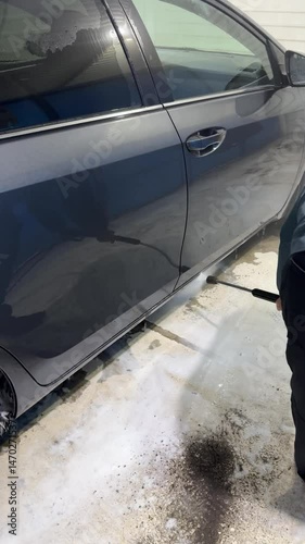 A man washes his car in a high pressure cleaning. He is washing his grey car in a self-service car wash. Vertical video