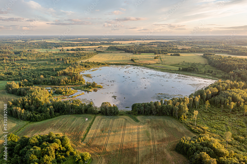 Obraz premium Vast landscape with tranquil lake surrounded by lush greenery and farmland at sunset