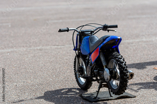 Miniature blue dirt bike on a stand in a parking lot during daylight