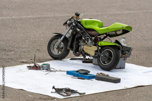 Small green motorcycle on a repair mat surrounded by tools and equipment