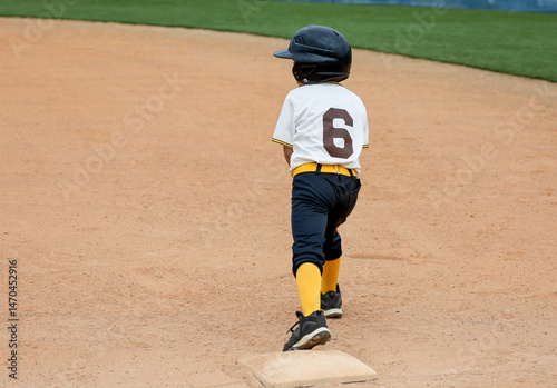 A six year old baseball player boy on first base ready to run.