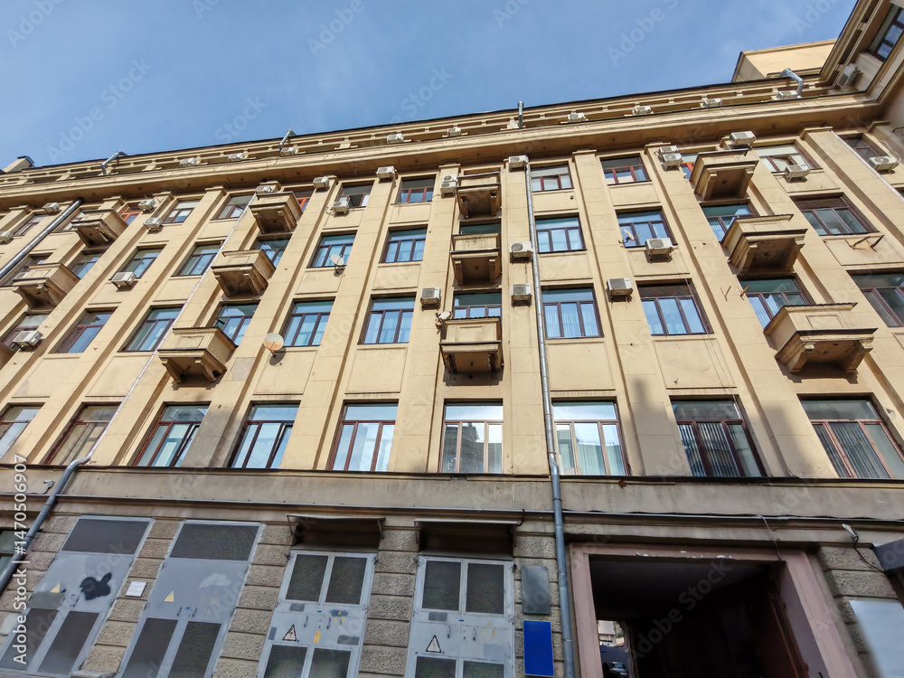 Fototapeta premium An upward view of a beige residential building with numerous windows, small balconies, and air conditioning units. The photo highlights urban density and the geometric symmetry of functional